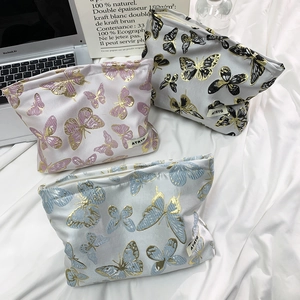 Detail of three butterfly embroidered cosmetic bags with woven texture and gold zipper