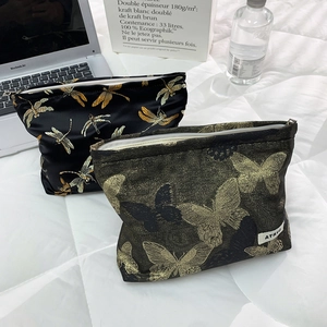 Detail of high-capacity butterfly makeup bags with gold zippers on a white quilted surface