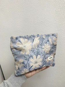 Detail of blue floral jacquard fabric and brand label on large travel makeup bag