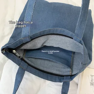 Detail view of the blue denim tote bag with a secure top zipper and internal small pocket