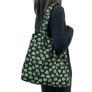 Large black corduroy tote bag with green heart prints worn by model for daily commute