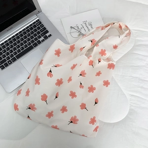 Flat lay of floral canvas tote bag next to a laptop on white bedding in soft light