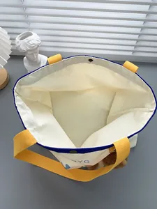 Detailansicht der beigen Canvas-Tasche mit Metalldruckknopf und gelben Tragegriffen