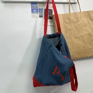 Detail of vintage denim tote bag showing red logo, contrast bottom, and zipper closure