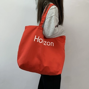 Detail of red canvas tote bag with white Horizon print shown on a model for daily commute