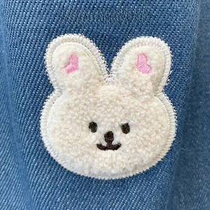 Close-up of white plush bunny embroidery patch on dark blue denim fabric with fine stitching