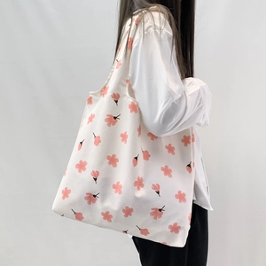Close-up of a white canvas tote bag featuring fresh pink floral prints and wide straps