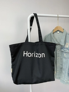 Detail of a large black canvas tote bag with white Horizon print and brand side label