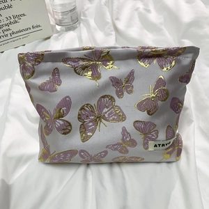 Detailed close-up of purple butterfly embroidery and gold stitching on a gray makeup bag