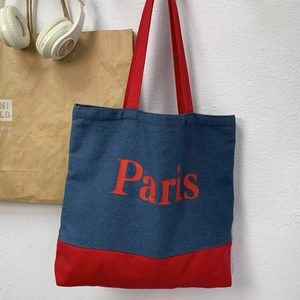Detail of blue denim tote bag with red handles and bold Paris letter print