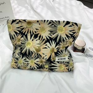 Macro detail of daisy floral cosmetics bag featuring quilted texture and brand label