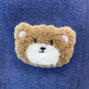 Close-up of cute plush bear embroidery with golden edge on dark blue denim fabric