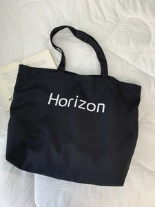 Close-up of black canvas tote bag with white Horizon print on a white quilted surface
