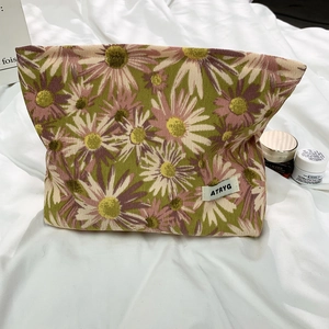 Detailed texture of daisy print makeup bag with a woven brand tag on green canvas fabric