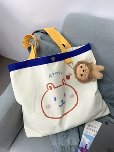 Süße Cartoon-Bär Segeltuchtasche mit blauem Rand und Löwen-Plüschanhänger auf Sofa