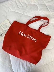 Close-up of red canvas tote bag with white Horizon print on a clean white background