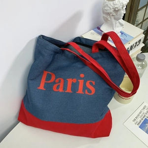 Detail of blue denim tote bag with red Paris print and handles on a white desk