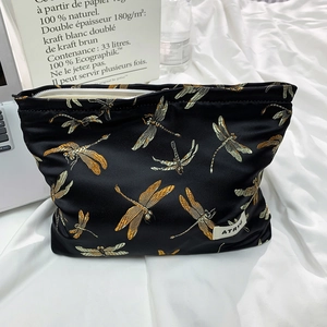 Macro view of black satin cosmetic bag with golden dragonfly embroidery and zipper detail