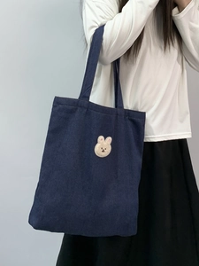 Detail view of a dark blue denim tote bag with a cute white rabbit embroidery on the front