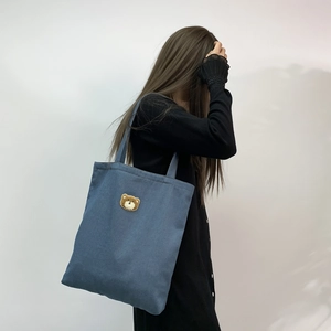 Detail of blue denim tote bag featuring a cute brown bear embroidery worn by a model