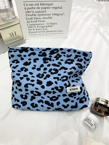 Detail of blue knitted leopard print makeup bag with zipper closure and brand label