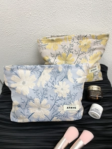 Detail showing two large jacquard floral cosmetic bags with toiletries on a textured background