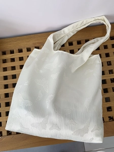 Macro shot of white textured tote bag with 3D butterfly embroidery on wooden bench