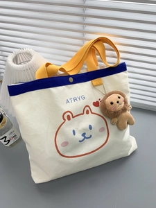 Detailaufnahme der beigen Segeltuchtasche mit Löwen-Plüschanhänger und gelben Griffen
