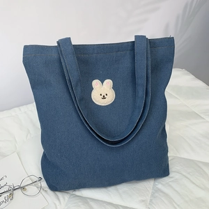 Detailed view of blue denim tote bag featuring cute beige plush rabbit embroidery