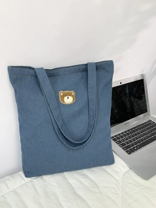 Detail shot of the cute brown plush bear embroidery on a blue denim tote bag surface