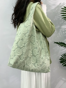 Detailed view of light green tote bag with rose embossed texture worn by a model