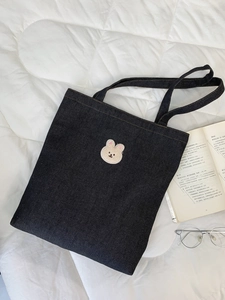Detailed view of navy denim tote bag with cute plush bear patch and shoulder straps