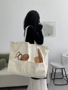 Detail of a large canvas tote bag with bread illustration and front pocket for daily use
