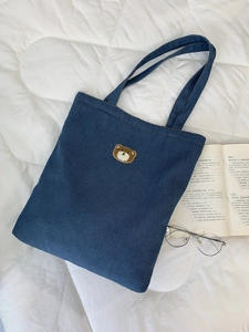 Detailed close-up of brown bear embroidery on a blue denim tote bag surface