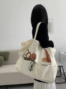 Close-up of a large canvas tote bag with bread print and a front pocket holding books