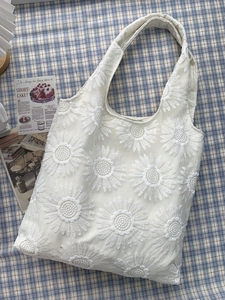 Détail de la broderie de marguerites sur un sac cabas en maille beige pour femme