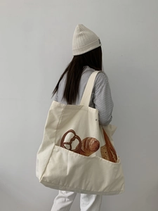 Detail of a large off-white canvas tote bag featuring bread prints and a front pocket