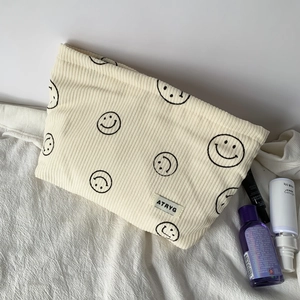 Detail of cream corduroy storage bag showing black smiley embroidery and soft texture