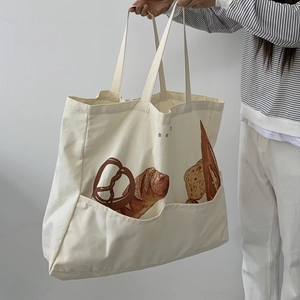 Detail of a beige canvas tote bag with bread print and functional double front pockets