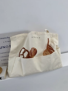 Detail of cream canvas tote bag featuring bread illustrations and large front pocket