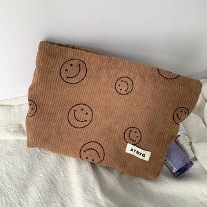 Detail of brown corduroy makeup bag with smiley face print and woven brand label