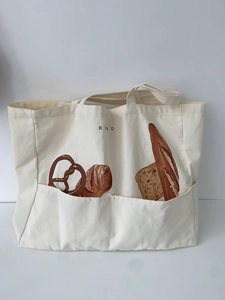 Detail view of large canvas tote bag featuring bread illustrations and front pockets
