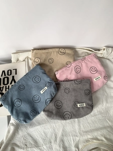 Close-up of corduroy makeup bags with smiley patterns in blue, grey, pink, and khaki colors