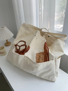 Large beige canvas tote bag with bread illustration and multiple pockets on white desk