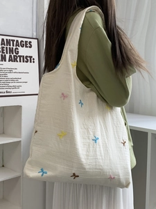 Detail of embroidered colorful bows on an off-white canvas tote bag worn on shoulder