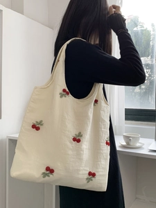 Detail of cream canvas tote bag with cherry embroidery on a model in a minimalist setting