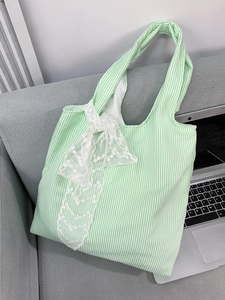 Detail of green striped canvas tote bag with white lace bow on a cozy sofa