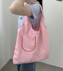 Detailed close-up of a pink nylon tote bag featuring a red gingham pocket and silver buckle