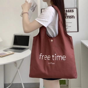 Detail of red canvas tote bag with free time coffee print shown on model shoulder