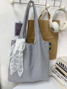 Detail of canvas tote bag with black stripes and a large white lace bow accessory